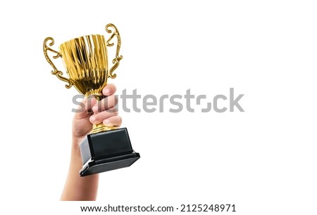 Shiny golden trophy cup in the hand of a child. Champion kid reward. Competition or contest prize. Royalty-Free Stock Photo #2125248971