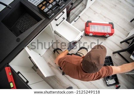 Cabinetmaker Specialist in His 40s Finishing Assembly of New Kitchen Cabinets Inside Modern Apartment Home. Royalty-Free Stock Photo #2125249118