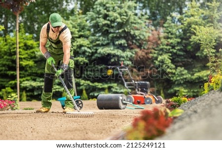 Caucasian Garden Specialist with Rake Preparing Soil For Natural Grass Turfs Installation. Landscaping Theme. Royalty-Free Stock Photo #2125249121