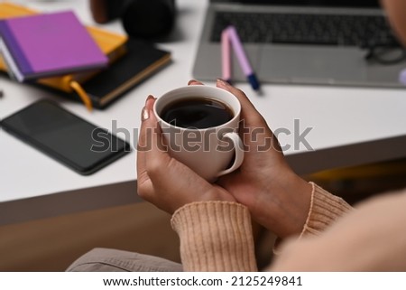 Young woman in warm sweater hands holding cup of hot coffee.