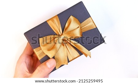 Man's hand holding a black gift box with a gold ribbon on a white background. Valentine concept, Christmas and Newyear concept. Anniversary and Thanksgiving concept.