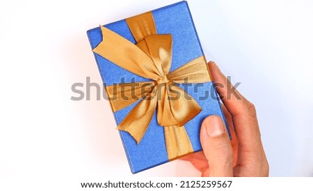 Man's hand holding a blue gift box with a gold ribbon on a white background. Valentine concept, Christmas and Newyear concept. Anniversary and Thanksgiving concept. FLat Lay. High Angle View.  