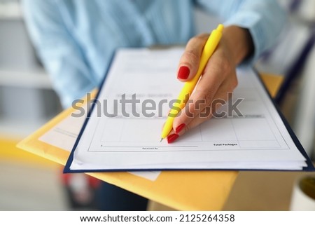 Female hands hold a package with a letter and a delivery document. A woman signs the receipt of a courier delivery