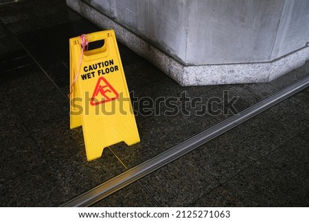 Yellow Caution slippery wet floor sign on the wet ground. Wet floor caution sign on walkway near the building after raining. Warning yellow plastic caution wet floor sign on the ground with copy space Royalty-Free Stock Photo #2125271063