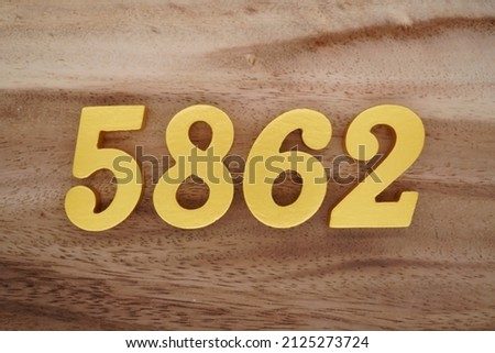 Wooden Arabic numerals 5862 painted in gold on a dark brown and white patterned plank background.