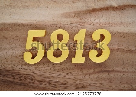 Wooden Arabic numerals 5813 painted in gold on a dark brown and white patterned plank background.