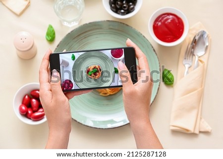 Woman taking picture of tasty Pasta Puttanesca in restaurant