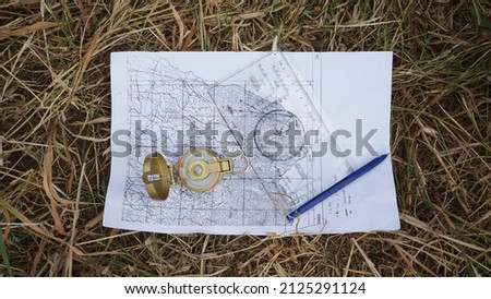 Compass, map, ruler and pencil on dry grass photographed from top angle.