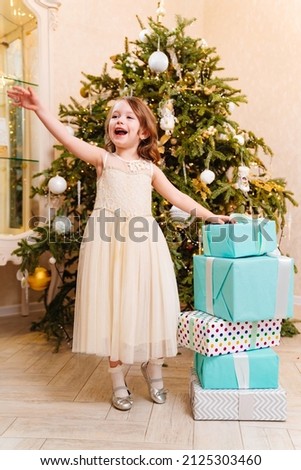 a happy little girl with boxes of gifts by the Christmas tree. the tradition of decorating the house and giving gifts for the new year. surprises for children. happy childhood.