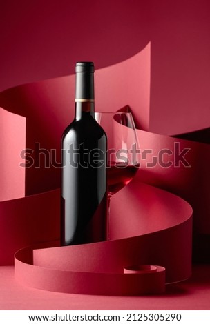 Bottle and glass of red wine on a red background.