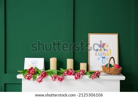 Basket with Easter eggs, candles, picture and tulips on mantelpiece near color wall