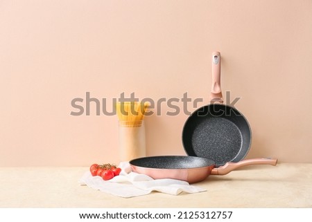 Frying pans and ingredients on light table against color wall Royalty-Free Stock Photo #2125312757