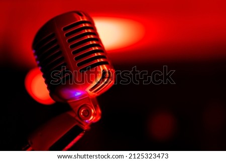 Classic stage microphone. Object illuminated with colored light. In the background, a view of blurred lights on the stage. Royalty-Free Stock Photo #2125323473