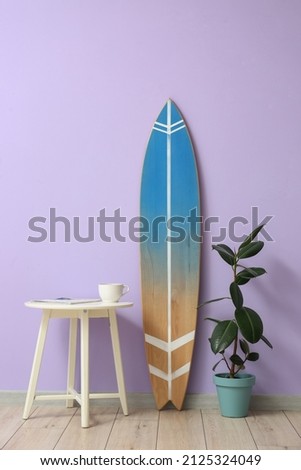 Interior of room with surfboard, houseplant and table near color wall