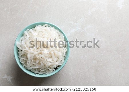 Bowl of tasty cooked rice noodles on light grey table, top view. Space for text