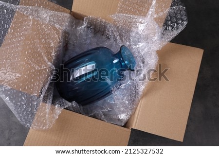Beautiful glass vase in box with bubble wrap on dark grey table, top view Royalty-Free Stock Photo #2125327532