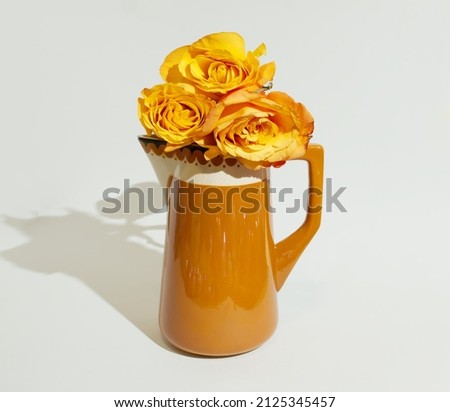 A brown jug with three orange roses on a beige background. Minimalist floral layout. Copy space. Flat lay. Minimalist concept of love. Anniversary or Valentine’s pattern.