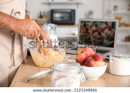 Young man preparing peach muffins while following cooking video tutorial in kitchen, closeup