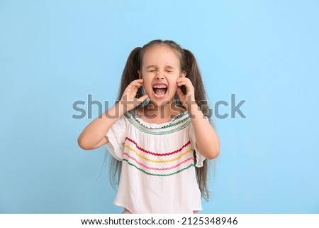 Portrait of angry little girl with ponytails on blue background