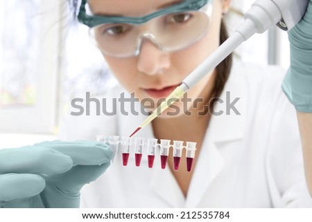 Young female scientist loads samples for DNA amplification by PCR into plastic tubes Royalty-Free Stock Photo #212535784