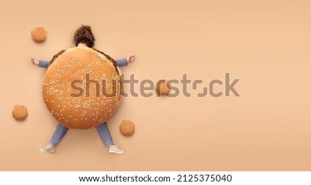 Girl with burger. Fast food concept, overweight. Minimal brown background with copy space. Top view Royalty-Free Stock Photo #2125375040