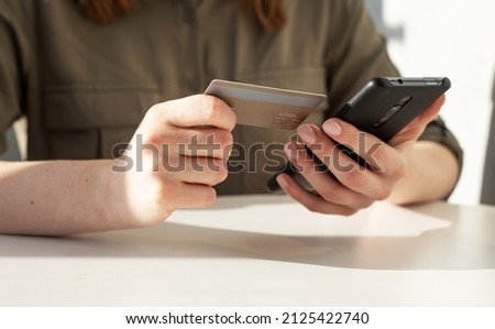 Woman hands closeup holding credit card and phone. Woman sitting at table and paying in application, shopping online or doing bank transaction. High quality photo
