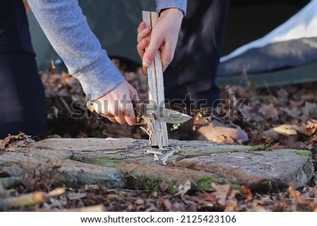 Close up of the hands of a caucasian woman splitting wood with a knife in the forest. Female outdoors collecting wood to start up a fire. Concept of bushcraft and outdoor survival.