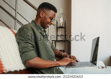 African American male student sitting on sofa typing on laptop studying for online exams  Royalty-Free Stock Photo #2125425653