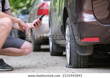 Driver calling road service for assistance having vehicle trouble with punctured flat tire on car parked on roadside Royalty-Free Stock Photo #2125445843