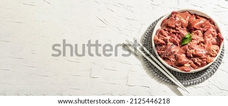 Raw chicken liver in a ceramic bowl. Fresh food ingredient with spices. Trendy hard light, dark shadow. White putty background, banner format