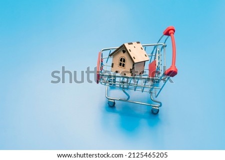 small wooden decorative house in a shopping cart on a blue background. purchase concept. High quality photo