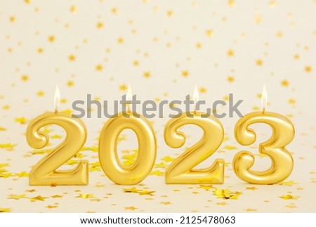gold-colored candles in the shape of numbers burn 2023 new year on a white background with stars postcard baner