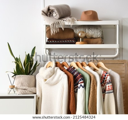 Rack with stylish knitted sweaters near light wall