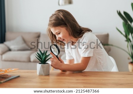 Little girl is sitting by the table with magnifying glass.