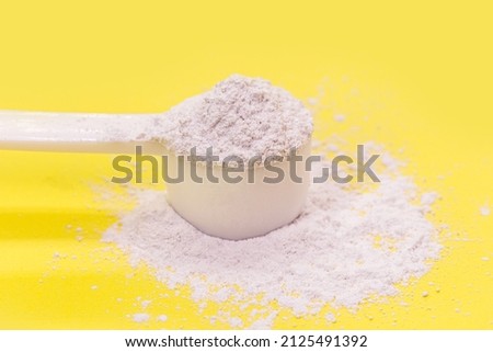 measuring spoon with casein or caffeine powder, food supplement, vitamin used by athletes, yellow background Royalty-Free Stock Photo #2125491392