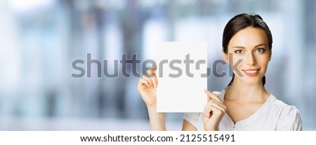 Portrait image of cheerful smiling woman in white cloth, holding showing demonstrate mock up mockup paper signboard, indoors. Business and advertising concept. Copy space empty free area for ad text.