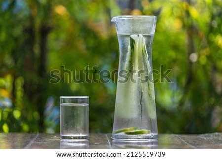 Water in glass with cucumber and lemon on wooden table in tropical cafe, Thailand, close up