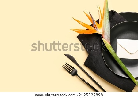 Simple table setting with bird of paradise flower and envelope on yellow background
