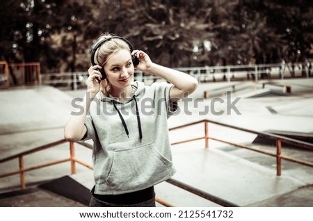 Young healthy fit blonde woman listening to music in stereo headphones outdoors