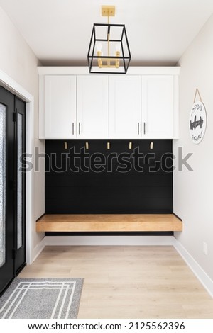 A modern farmhouse entryway with bench seating, black shiplap, white cabinets, gold coat hooks, black and gold light fixture, and homemade welcome sign hanging.