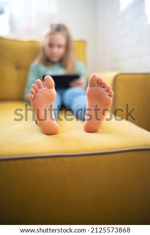 girl sits on the sofa and uses the digital tablet computer. close-up of the legs of the heels of the child, the rest is out of focus