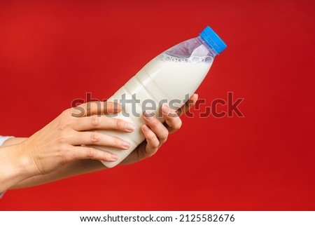 Close-up photo of the bottle with milk in woman's hand. Healthy eating concept. Isolated over red background. 