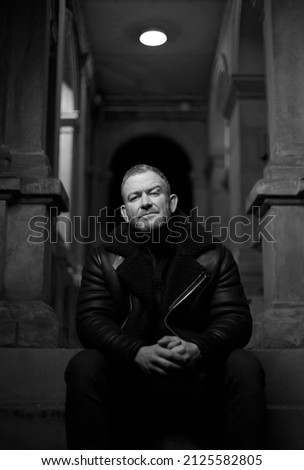 Caucasian male sits on steps with chin up slightly and looking into camera.