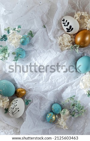 Easter eggs with candy and flowers with copy space on white paper. Happy Easter card.  White, blue and golden eggs on  wrapping paper