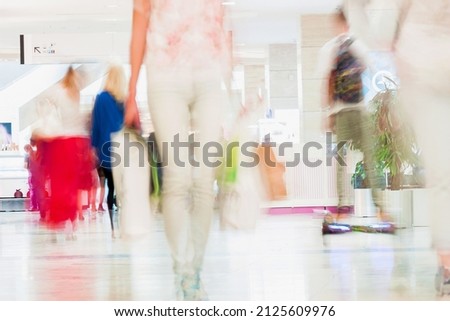 Abstract defocused motion blurred young people walking in the shopping center. Beautiful figure of a girl with shopping bags close-up. For background , backdrop, substrate, composition use.