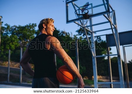 Back view young serious confident sporty sportsman man 20s wear sports clothes training hold in hand ball play at basketball game playground court on sky background. Outdoor courtyard sport concept.