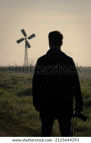 A man with a camera admires the view of a windmill with a sunrise