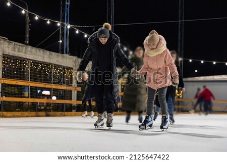mother and daughter skate on the ice rink in the evening