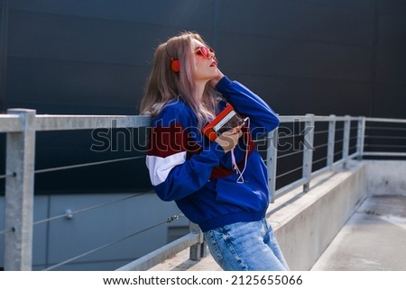 modern retro style 90s, girl in a blue sports jacket, cassette player, listening to music, urban style mood Royalty-Free Stock Photo #2125655066