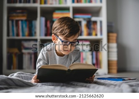 One caucasian boy lying on the floor at home in day reading a book front view wearing eyeglasses copy space real people Royalty-Free Stock Photo #2125662620
